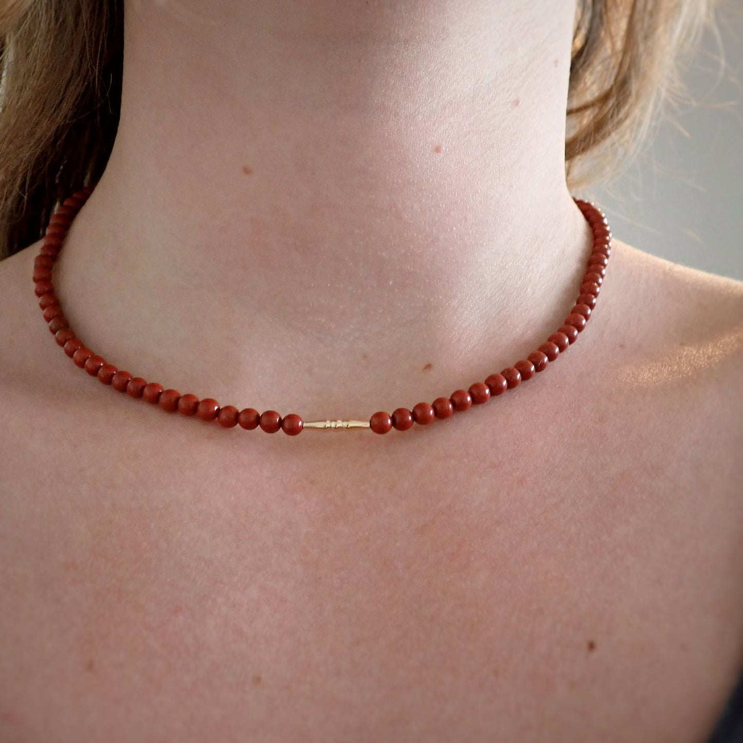 dame met korte rode ketting van natuursteen met een goud staafje in het midden