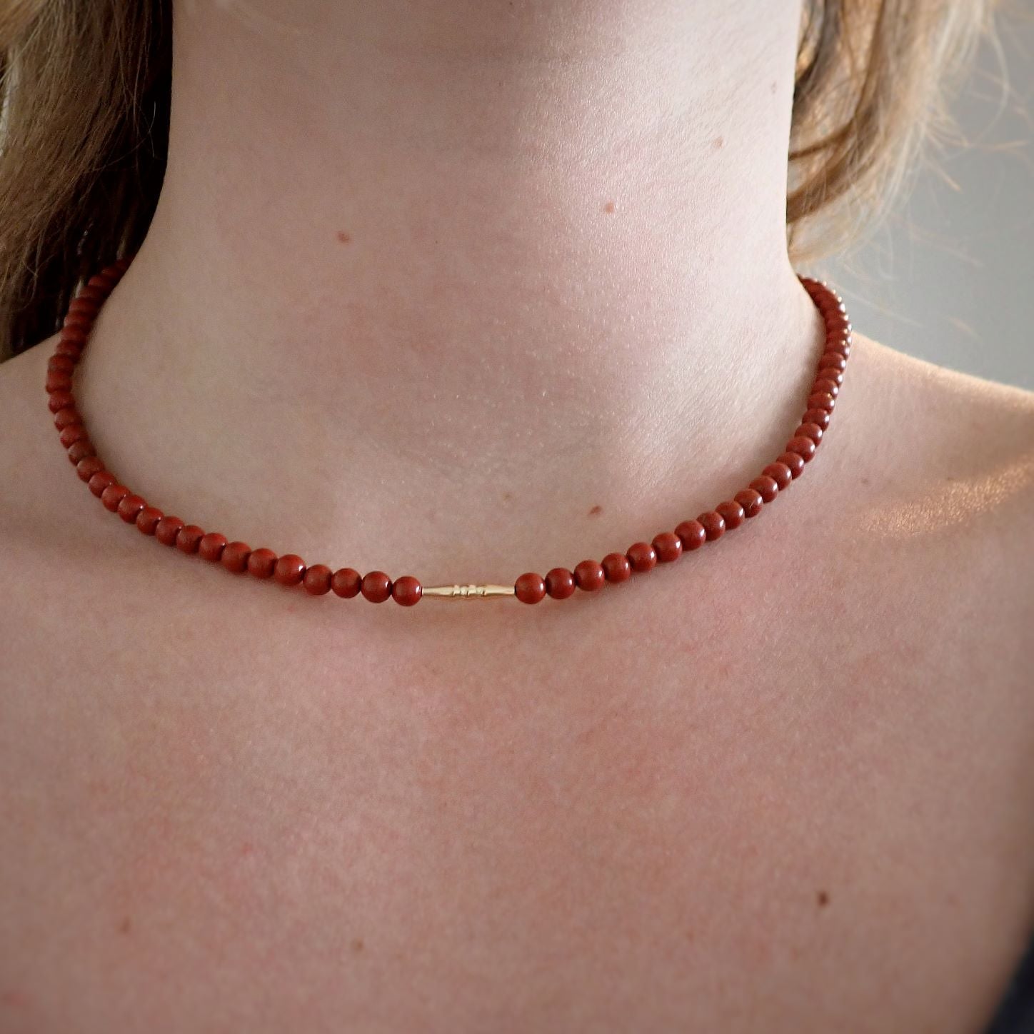 dame met korte rode ketting van natuursteen met een goud staafje in het midden