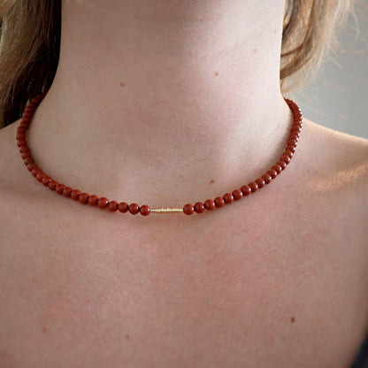 dame met korte rode ketting van natuursteen met een goud staafje in het midden