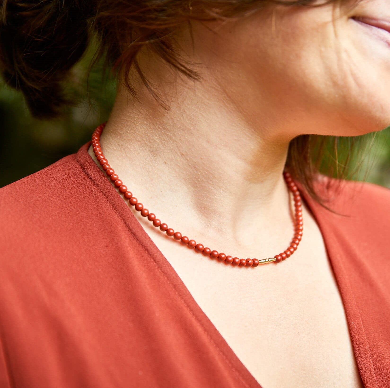 vrouw met rode jurk en bijpassend sieraad collier van rode jaspis stenen en goud